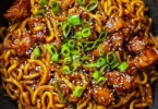Bowl of Korean spicy chicken noodles garnished with green onions and chili flakes