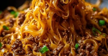 A vibrant dish of Mongolian ground beef noodles topped with fresh vegetables.
