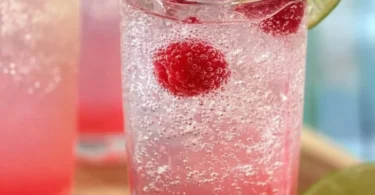 A glass of Raspberry Key Lime Italian Soda with lime slices and raspberries