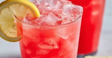 A refreshing glass of watermelon lemonade with ice and mint leaves.